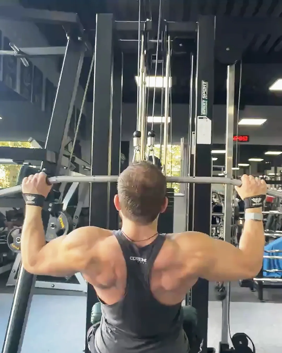 V from behind, mid-rep on the lat pulldown in the gym, during a live stream on 15 September 2026.